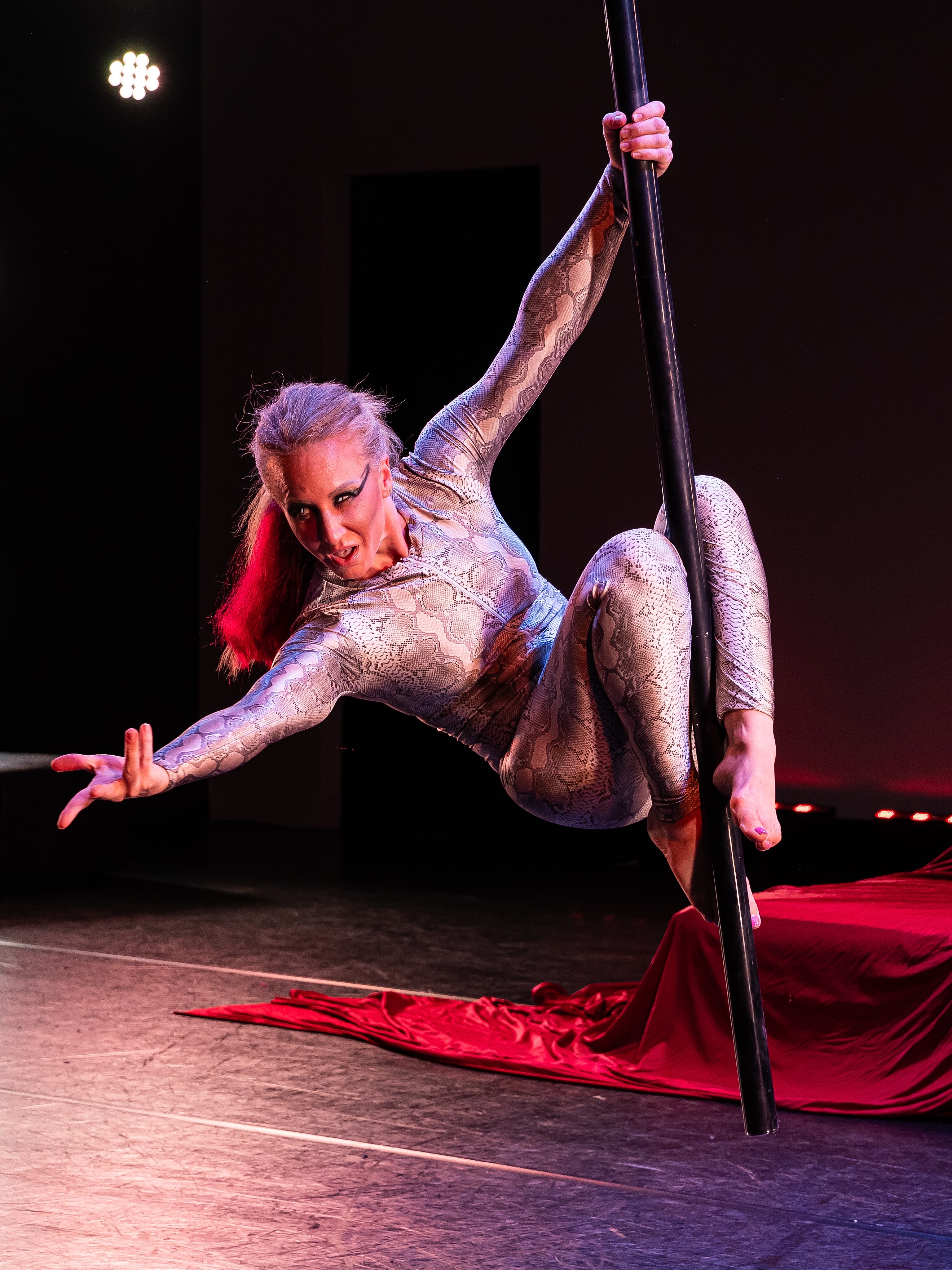April in a dramatic aerial pole pose with red stage fabric